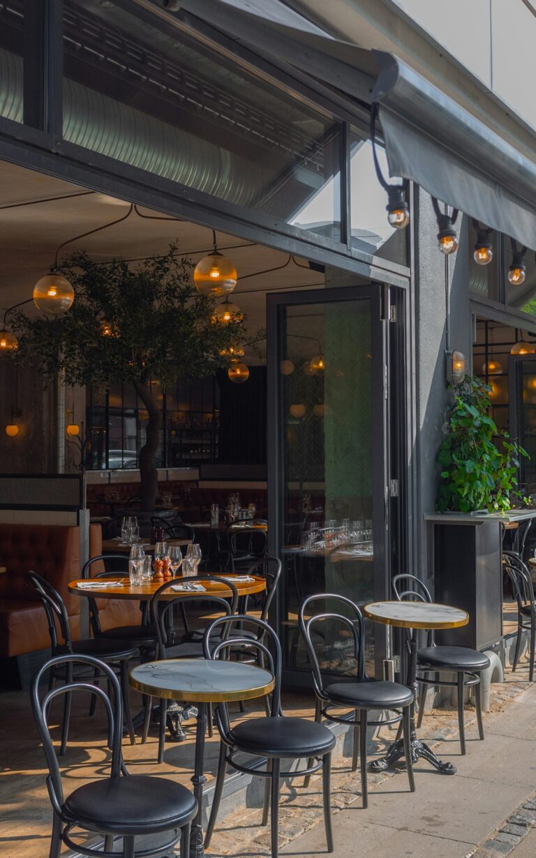 Tables and chairs on a restaurant patio with an open glass storefront