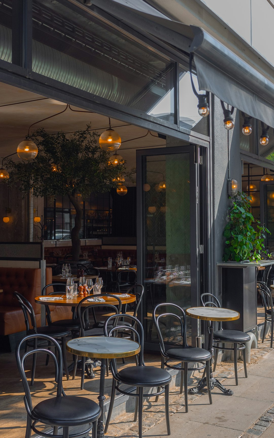 Tables and chairs on a restaurant patio with an open glass storefront